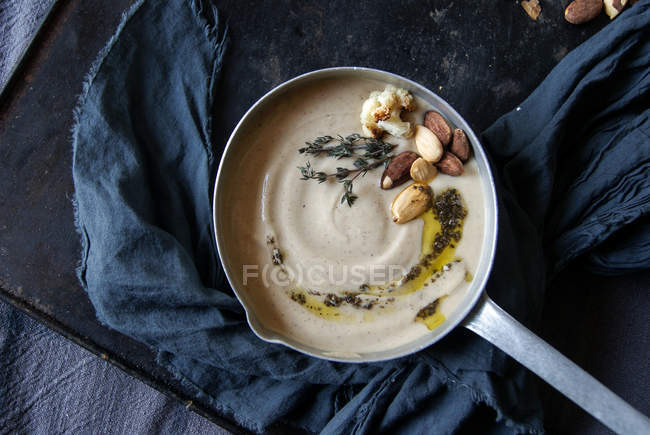 Creamy cauliflower soup with almonds in saucepan on tray with cloth — Stock Photo