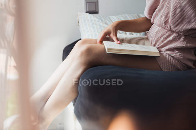 Крупним планом жінка з книгою, що сидить на ліжку на сонячному світлі — стокове фото