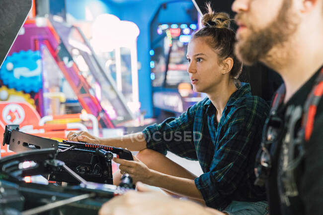 Вид сбоку красивой молодой женщины, сидящей рядом с мужчиной и играющей в аркадную игру — стоковое фото