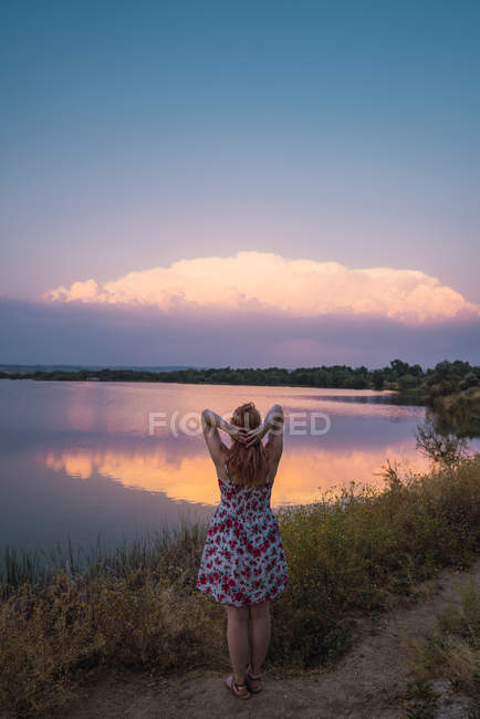 Donna in abito estivo in piedi sulla riva del lago al tramonto — Foto stock