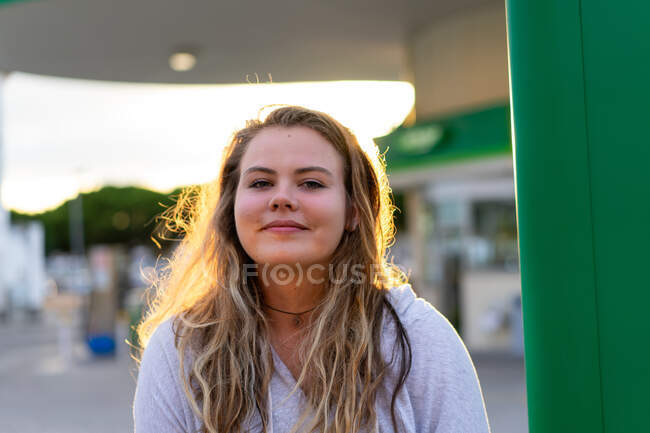 Felice giovane donna in abito casual guardando la fotocamera e ridendo in retroilluminato di luce del tramonto — Foto stock