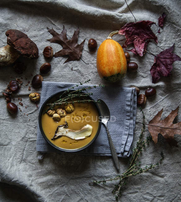 Kürbiscremesuppe serviert in Schüssel mit Zutaten auf rustikalem Stoff mit Herbstblättern — Stockfoto