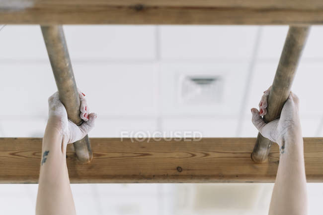 Manos de mujer irreconocible agarrando tablones de madera en el gimnasio mientras realiza pull-ups durante el entrenamiento - foto de stock