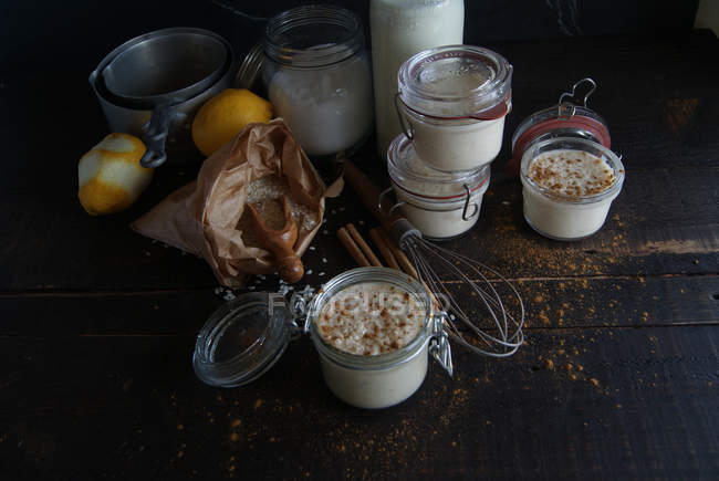 Скляні банки з солодким десертом рису з молоком та корицею на дерев'яному столі з інгредієнтами — стокове фото