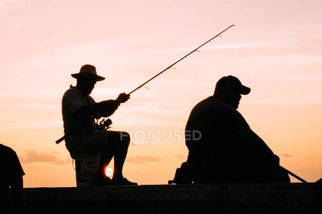 Silhueta preta de homens que pescam à beira-mar contra o céu pôr-do-sol luz, Cuba. — Fotografia de Stock