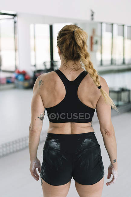 Back view of female athlete with hands covered with chalk standing in gym during training — Stock Photo
