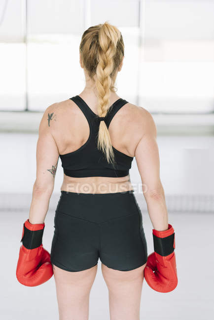 Вид ззаду на м'язисту жінку в рукавичках червоного боксу, що стоять у спортзалі — стокове фото