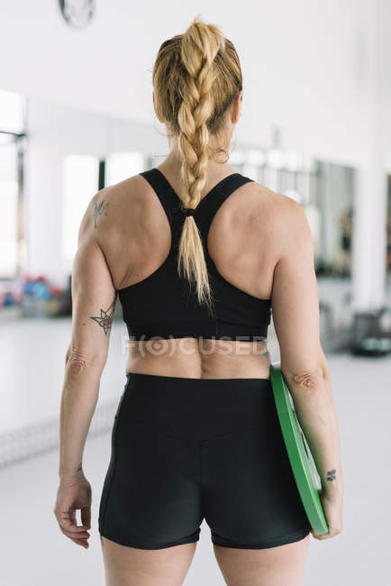 Female athlete in black sportswear holding heavy disc in gym — Stock Photo