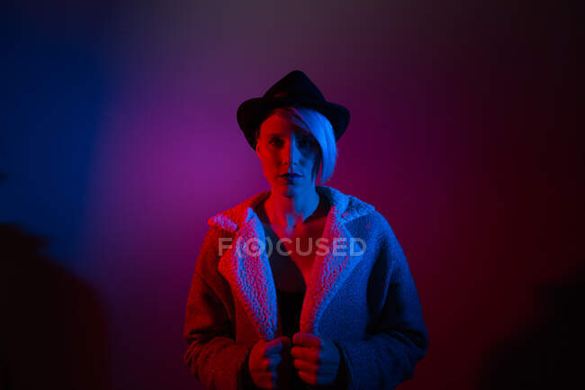 Atractiva mujer con sombrero de disparar en el estudio con luces azules y rojas - foto de stock