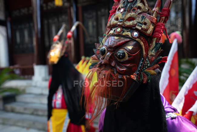 Gruppo di minoranza etnica Miao femmine in costumi tradizionali luminosi e maschere in piedi con l'uomo in costume giallo all'aperto al muro dell'edificio cinese nel Guizhou — Foto stock