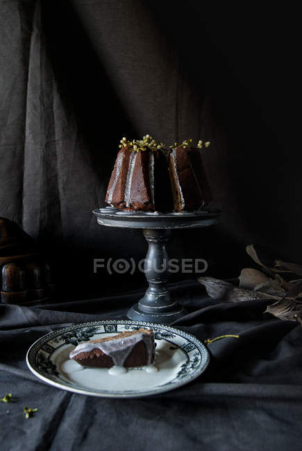 Bundt Vegan шоколадний торт, прикрашений гілки рослини на стенді торт з шматок на плиті на чорний тканина — стокове фото
