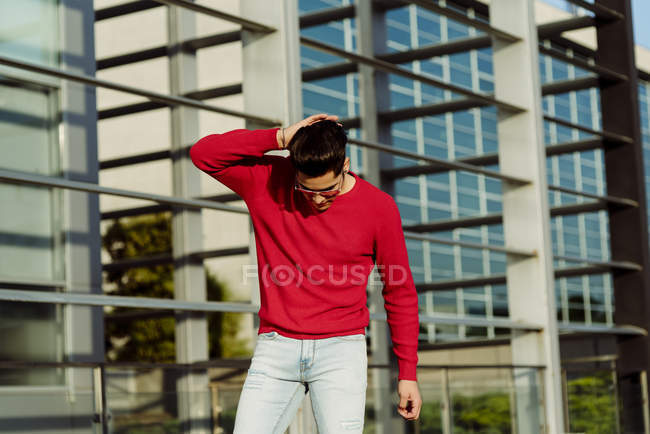 Jovem atraente em pulôver vermelho em pé na frente do edifício — Fotografia de Stock