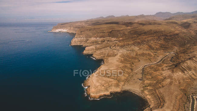 Barren rocky cliffs on shore of calm dark sea, Gran Canaria, Spain — Stock Photo
