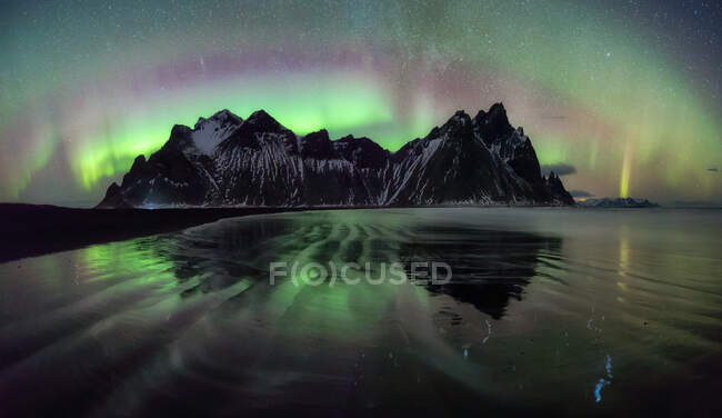 Picturesque view of frozen surface of water and small mountain ridge on background of amazing polar lights in Iceland. — Stock Photo