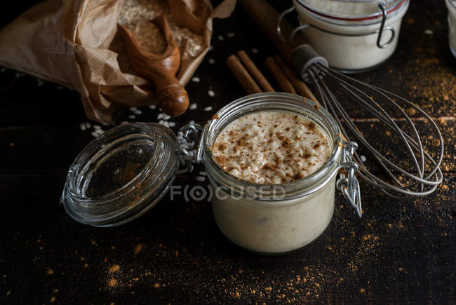 Glass jars of sweet dessert of rice with milk and cinnamon on wooden table with ingredients — Stock Photo