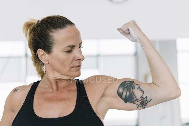 Strong woman showing biceps of tattooed arm in gym — Stock Photo