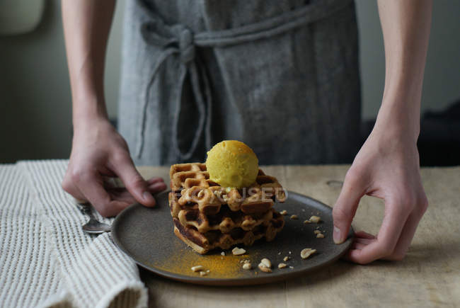 Mãos humanas segurando waffles com banana e sorvete de caril no prato — Fotografia de Stock