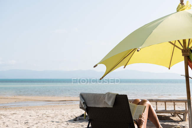 Pessoa sentada na espreguiçadeira e ler livro na praia — Fotografia de Stock