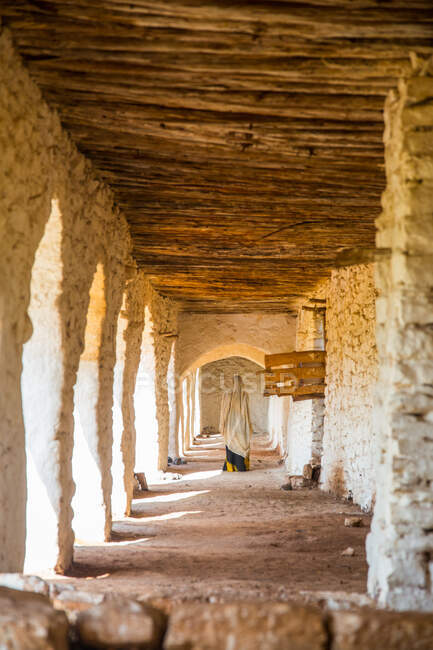 Задний вид женщины в хиджабе идущей по коридору с каменными арками и деревянным потолком — стоковое фото