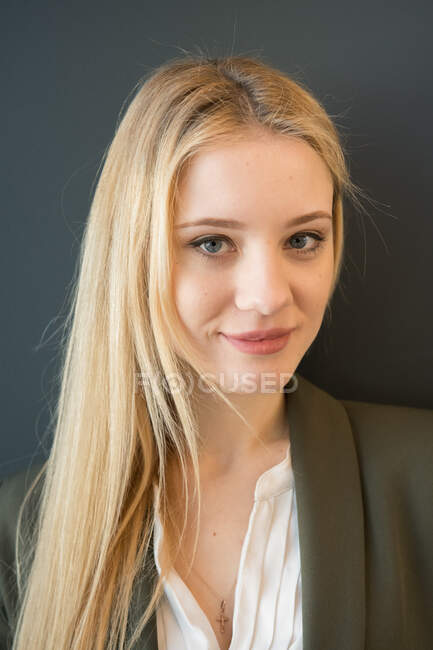 Beautiful blond young woman in dark elegant suit standing confidently with crossed arms and looking at camera smiling on black background — Stock Photo