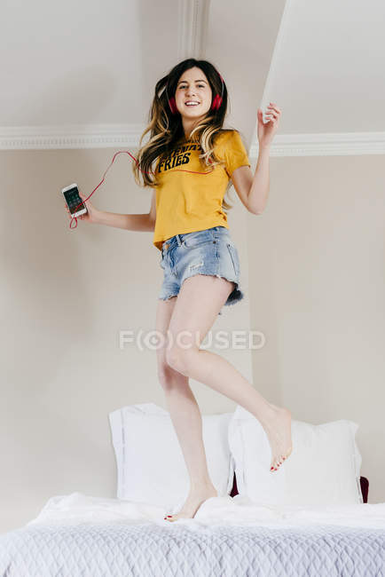Girl dancing on bed with smartphone and headphones — Stock Photo