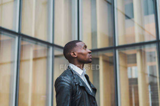 Впевнений етнічний чоловік стоїть проти скляної будівлі і дивиться в сторону — стокове фото