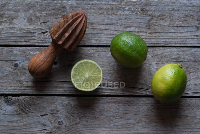 Fresh whole and halved limes with wooden squeezer on grey wood — Stock Photo