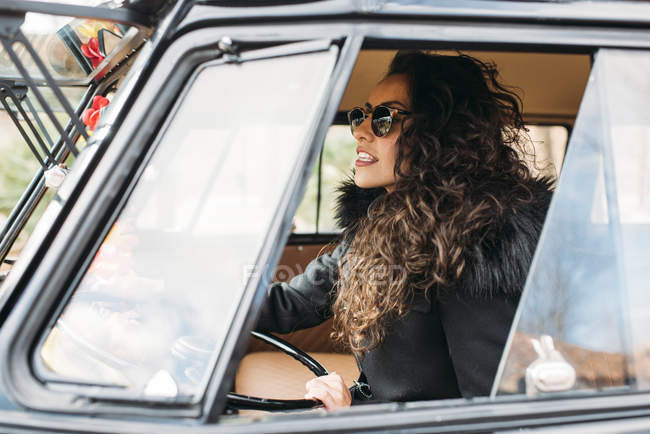 Молодая женщина в черном пальто и солнцезащитных очках сидит внутри автомобиля — стоковое фото