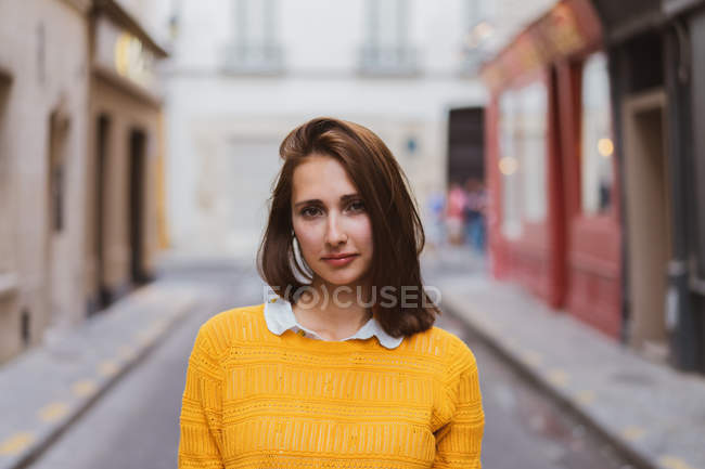 Красивая женщина в жёлтом кардигане стоит на улице и смотрит в камеру. — стоковое фото