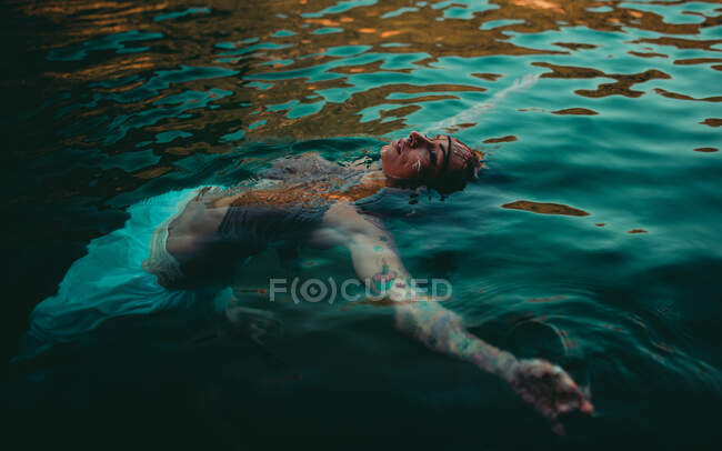 Jovem atraente com desenhos tradicionais indianos no rosto relaxante na água com os olhos fechados — Fotografia de Stock