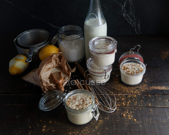 Стеклянные банки со сладким десертом риса с молоком и корицей на деревянном столе с ингредиентами — стоковое фото