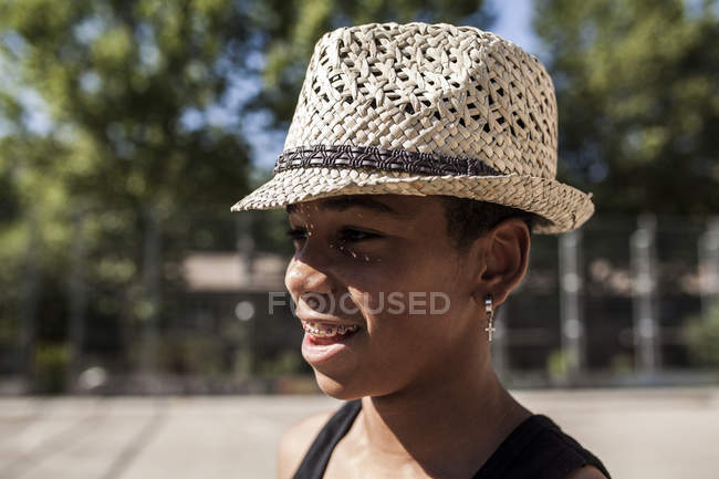 Улыбающийся мальчик в соломенной шляпе стоит на улице и смотрит в сторону — стоковое фото