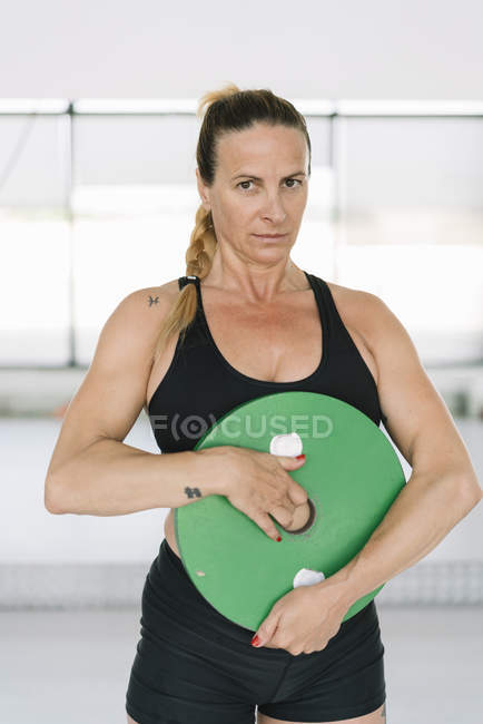 Atleta donna in abbigliamento sportivo nero che tiene il disco pesante e fa esercizi durante l'allenamento in palestra — Foto stock