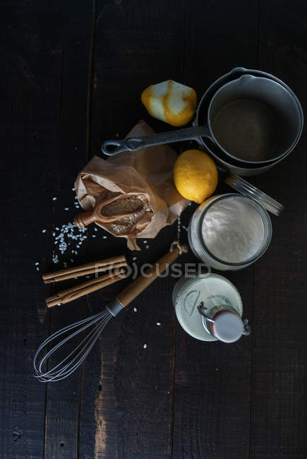 Arreglo rústico de arroz, leche, especias y limones sobre mesa de madera negra con utensilio — Stock Photo