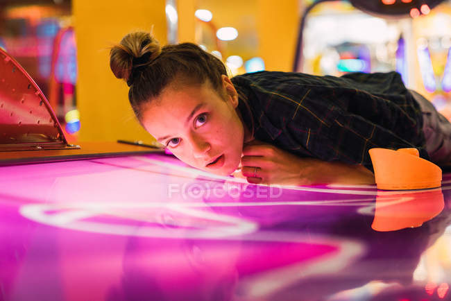 Charming young woman in casual outfit lying on shiny table for air hockey and looking at camera — Stock Photo