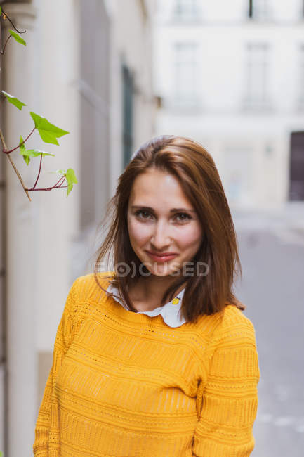 Досить усміхнена жінка в жовтому кардигані дивиться на камеру на вулиці — стокове фото