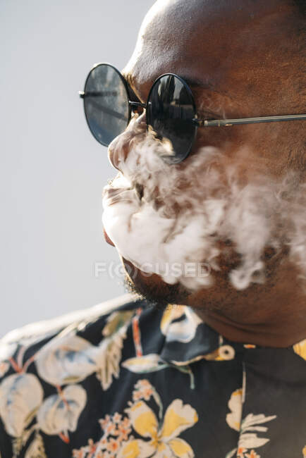Uomo nero elegante con gli occhiali da sole. Sta vaporizzando con una sigaretta elettronica all'aperto — Foto stock