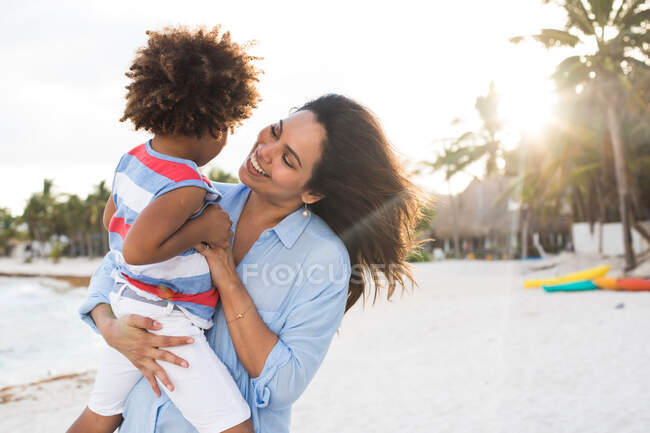 Mulher étnica feliz com criança na praia — Fotografia de Stock