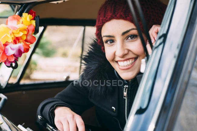 Sonriente mujer joven en ropa de abrigo sentado dentro del coche y mirando a la cámara - foto de stock