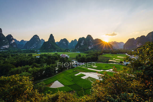 Campos e cidade cercada por montanhas rochosas únicas ao pôr do sol, Guangxi, China — Fotografia de Stock