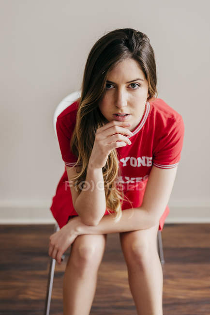 Bella donna in abito rosso seduto sulla sedia e fissando la fotocamera — Foto stock