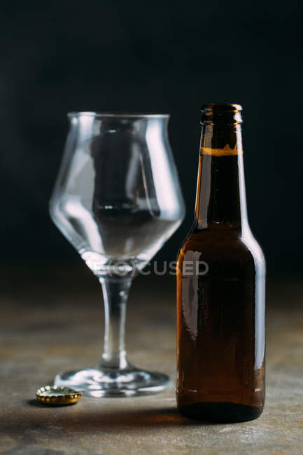 Beer bottle and empty glass on grey background — Stock Photo