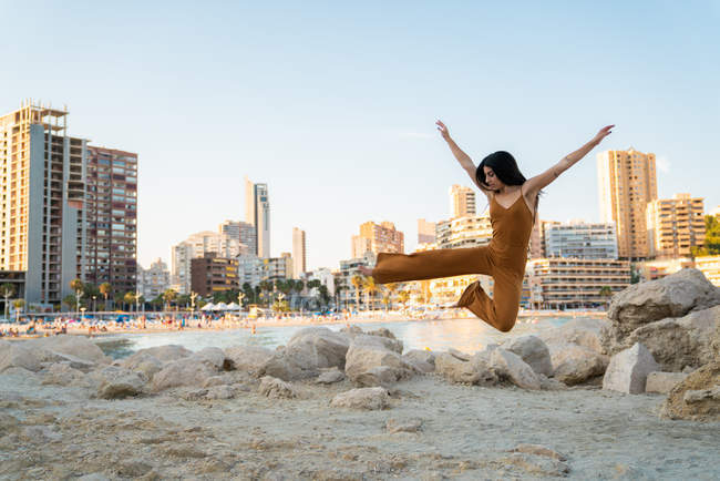 Playful woman in stylish overall making splits on shore with buildings on background — Stock Photo