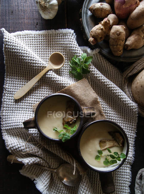 Bowls of tasty Jerusalem artichoke soup with ingredients on rustic wooden table — Stock Photo
