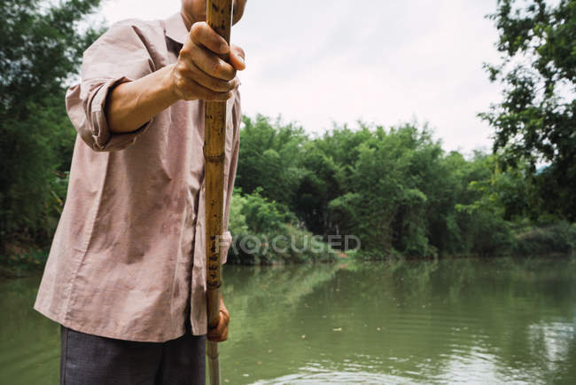 Man holding paddle and standing on river with trees and bushes on background — Stock Photo