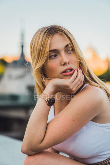 Blonde junge Frau in lässigem Outfit blickt in die Kamera, während sie in der Stadt sitzt — Stockfoto
