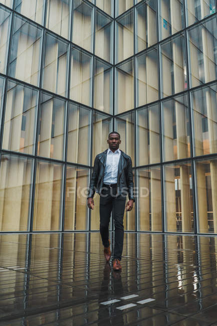 Uomo d'affari che cammina sul marciapiede contro l'edificio in vetro moderno — Foto stock