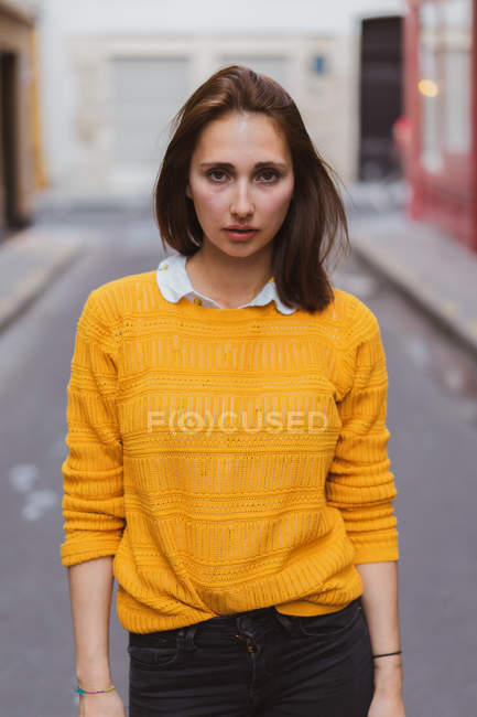 Pretty Woman In Yellow Cardigan Standing On Street And Looking At Camera Focus On Foreground