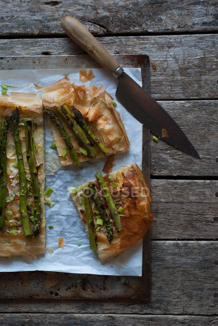 Baked asparagus pie on wooden surface with knife — Stock Photo