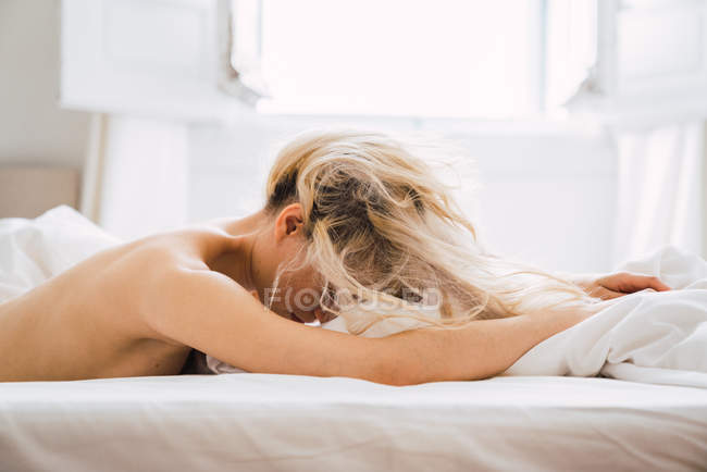 Donna bionda nuda sdraiata su un letto comodo in camera da letto accogliente — Foto stock